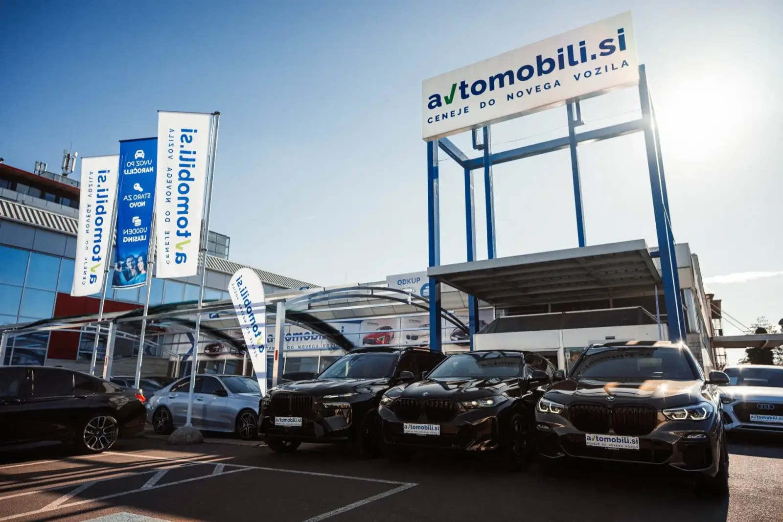 Zunanjost avtohiše Avtomobili.si v Mariboru z vozili BMW pred vhodom in zastavami